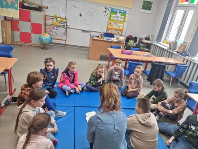 Na zdjęciach znajdują się uczestnicy zajęć. Dzieci siedzą w kręgu na materacach.