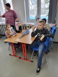 Na zdjęciach znajdują się uczestnicy zajęć. Dzieci siedzą przy stole i wykonują prace plastyczne.