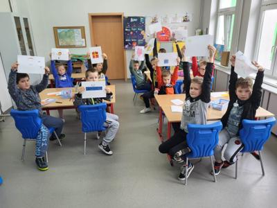 Na zdjęciu znajdują się uczestnicy zajęć. Dzieci trzymają w ręce prace plastyczne.