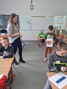Na zdjęciu znajdują się uczestnicy zajęć. Dziecko pokazuje wykonaną prace plastyczną.