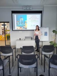 Na zdjęciu znajduje się prowadząca warsztat. W tle wyświetlana prezentacja multimedialna. Zdjęcie wykonano w w bibliotece w sali wielofunkcyjnej.
