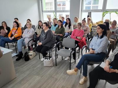 Na zdjęciu znajdują się uczestnicy warsztatów, którzy siedzą na krzesłach. Zdjęcie wykonano w w bibliotece w sali wielofunkcyjnej.