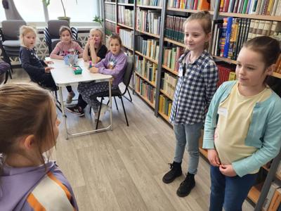 Na zdjęciu znajdują się uczestnicy zajęć. Dzieci wykonują zadania. Zdjęcie wykonano w sali wielofunkcyjnej biblioteki.