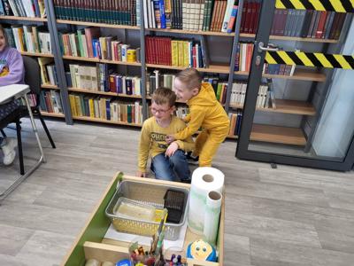 Na zdjęciu znajdują się uczestnicy zajęć. Dzieci wykonują zadania. Zdjęcie wykonano w sali wielofunkcyjnej biblioteki.
