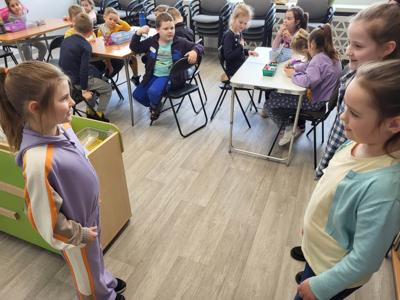 Na zdjęciu znajdują się uczestnicy zajęć. Dzieci wykonują zadania. Zdjęcie wykonano w sali wielofunkcyjnej biblioteki.