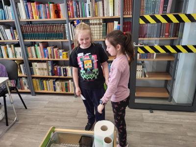 Na zdjęciu znajdują się uczestnicy zajęć. Dzieci wykonują zadania. Zdjęcie wykonano w sali wielofunkcyjnej biblioteki.