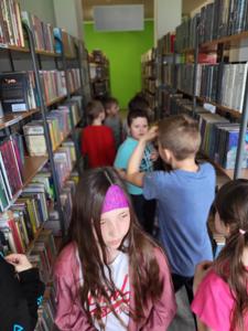Na zdjęciu znajdują się uczestnicy warsztatów. Dzieci wykonują zadania.  W tle księgozbiór biblioteki.
