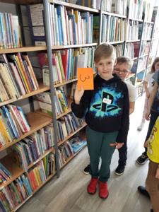 Na zdjęciu znajdują się uczestnicy warsztatów. Dzieci wykonują zadania.  W tle księgozbiór biblioteki.