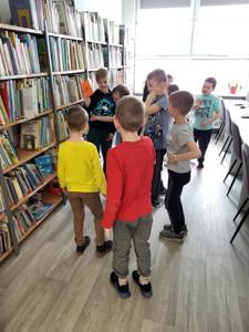 Na zdjęciu znajdują się uczestnicy warsztatów. Dzieci wykonują zadania.  W tle księgozbiór biblioteki.