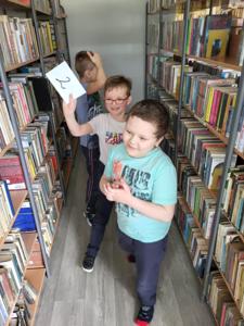 Na zdjęciu znajdują się uczestnicy warsztatów. Dzieci wykonują zadania.  W tle księgozbiór biblioteki.