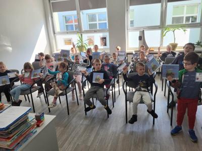 Na zdjęciu znajdują się uczestnicy zajęć. Dzieci siedzą na krzesłach w rękach trzymają książki i dyplomy.
