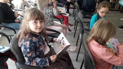 Na zdjęciu znajdują się uczestnicy zajęć. Dzieci siedzą na krzesłach. Zdjęcie wykonano w sali wielofunkcyjnej biblioteki.