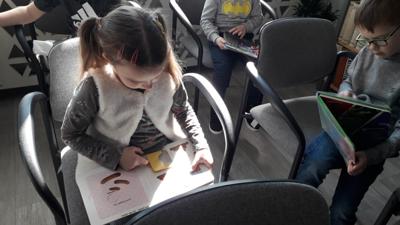 Na zdjęciu znajdują się uczestnicy zajęć. Dzieci siedzą na krzesłach. Zdjęcie wykonano w sali wielofunkcyjnej biblioteki.
