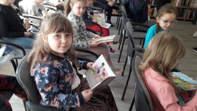 Na zdjęciu znajdują się uczestnicy zajęć. Dzieci siedzą na krzesłach. Zdjęcie wykonano w sali wielofunkcyjnej biblioteki.