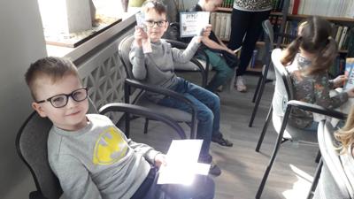 Na zdjęciu znajdują się uczestnicy zajęć. Dzieci siedzą na krzesłach. Zdjęcie wykonano w sali wielofunkcyjnej biblioteki.