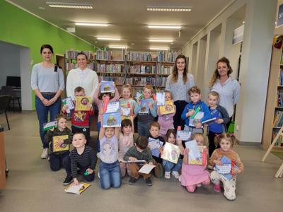 Na zdjęciu znajdują się uczestnicy zajęć. Dzieci trzymają w rękach dyplomy i książki. Zdjęcie wykonano w bibliotece.