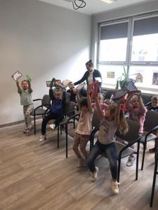 Na zdjęciu znajdują się uczestnicy zajęć. Dzieci siedzą na krzesłach. Zdjęcie wykonano w bibliotece.