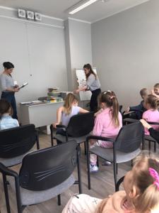 Na zdjęciu znajdują się uczestnicy zajęć. Dzieci siedzą na krzesłach. Zdjęcie wykonano w bibliotece.