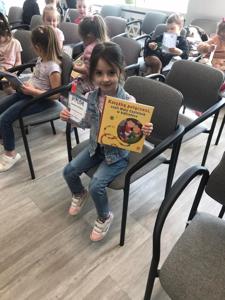 Na zdjęciu znajdują się uczestnicy zajęć. Dzieci siedzą na krzesłach. Zdjęcie wykonano w bibliotece.