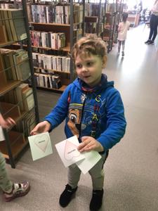 Na zdjęciu znajdują się uczestnicy zajęć. Dzieci trzymają w rękach dyplomy i książki. Zdjęcie wykonano w bibliotece.