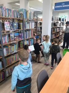 Na zdjęciu znajdują się uczestnicy zajęć. Dzieci trzymają w rękach dyplomy i książki. Zdjęcie wykonano w bibliotece.