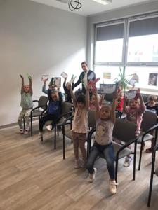 Na zdjęciu znajdują się uczestnicy zajęć. Dzieci siedzą na krzesłach. Zdjęcie wykonano w bibliotece.