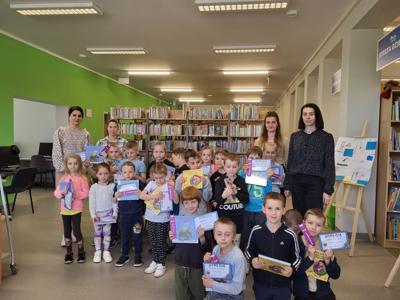 Na zdjęciu znajdują się uczestnicy pasowania. Dzieci trzymają  w rękach dyplomy i książki. Zdjęcie wykonano w bibliotece.