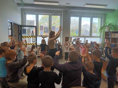 Na zdjęciu znajdują się uczestnicy pasowania. Dzieci stoją w kółku i wykonują zadania. Zdjęcie wykonano w bibliotece.