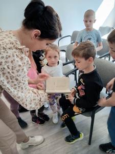 Na zdjęciu znajdują się uczestnicy pasowania. Dzieci siedzą na krzesłach. Zdjęcie wykonano w bibliotece.