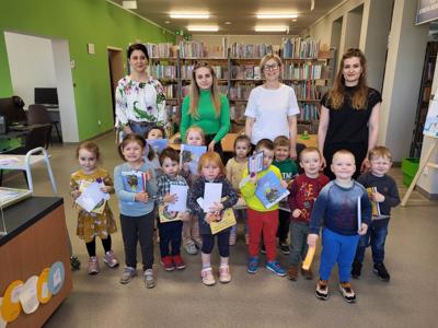 Na zdjęciu znajdują się uczestnicy pasowanie. Dzieci trzymają w rękach dyplomy i książki. Zdjęcie wykonano w bibliotece.