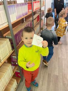 Na zdjęciu znajdują się uczestnicy pasowania. Dzieci znajdują się pomiędzy regałami z książkami. Zdjęcie wykonano w bibliotece.