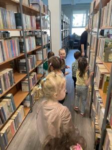 Na zdjęciu znajdują się uczestnicy pasowania. Dzieci znajdują się pomiędzy regałami z książkami. Zdjęcie wykonano w bibliotece.