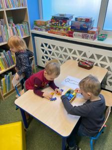 Na zdjęciu znajdują się uczestnicy pasowania. Dzieci znajdują się pomiędzy regałami z książkami. Zdjęcie wykonano w bibliotece.