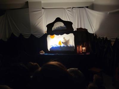 Na zdjęciu znajdują się uczestnicy przedstawienia. Dzieci i rodzice siedzą na krzesłach i poduszkach. W tle scenka teatralna.
