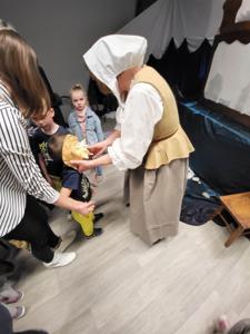 Na zdjęciu znajdują się uczestnicy przedstawienia. Dzieci i rodzice siedzą na krzesłach i poduszkach. W tle scenka teatralna.