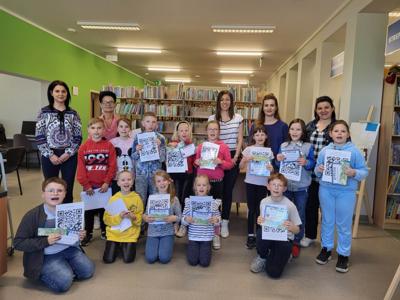 Na zdjęciu znajdują się uczestnicy zajęć. Dzieci trzymają w rękach dyplomy. Zdjęcie wykonano w bibliotece.