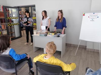 Na zdjęciu znajdują się uczestnicy zajęć. Dzieci siedzą na krzesłach. Zdjęcie wykonano w bibliotece.
