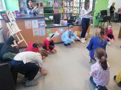 Na zdjęciu znajdują się uczestnicy zajęć. Dzieci wykonują zadania w kręgu. Zdjęcie wykonano w bibliotece.