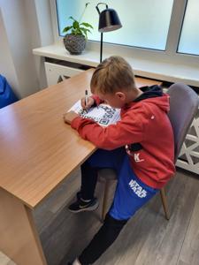 Na zdjęciu znajdują się uczestnicy zajęć. Dzieci siedzą na krzesłach. Zdjęcie wykonano w bibliotece.