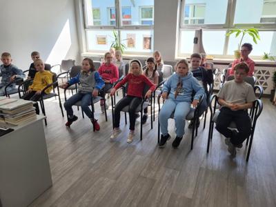 Na zdjęciu znajdują się uczestnicy zajęć. Dzieci siedzą na krzesłach. Zdjęcie wykonano w bibliotece.
