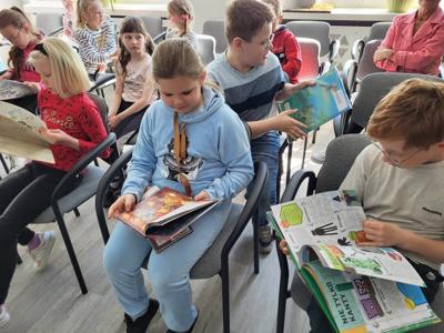 Na zdjęciu znajdują się uczestnicy zajęć. Dzieci siedzą na krzesłach. Zdjęcie wykonano w bibliotece.