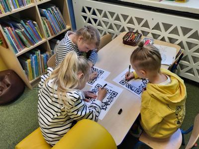 Na zdjęciu znajdują się uczestnicy zajęć. Dzieci siedzą na krzesłach. Zdjęcie wykonano w bibliotece.
