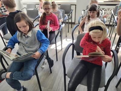 Na zdjęciu znajdują się uczestnicy zajęć. Dzieci siedzą na krzesłach. Zdjęcie wykonano w bibliotece.