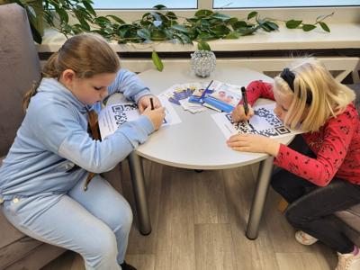 Na zdjęciu znajdują się uczestnicy zajęć. Dzieci siedzą na krzesłach. Zdjęcie wykonano w bibliotece.