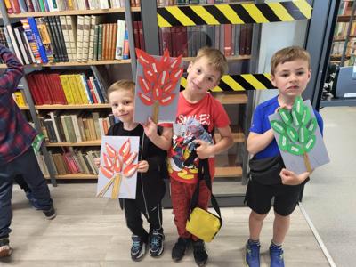Na zdjęciu znajdują się uczestnicy warsztatów. Dzieci trzymają w rękach prace plastyczne. Zdjęcie wykonano w bibliotece.