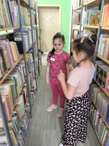 Na zdjęciu znajdują się uczestnicy warsztatów. Dzieci stoją i wykonują zadania. Zdjęcie wykonano w bibliotece.