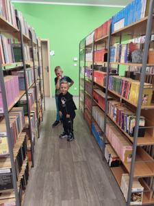 Na zdjęciu znajdują się uczestnicy warsztatów. Dzieci stoją i wykonują zadania. Zdjęcie wykonano w bibliotece.