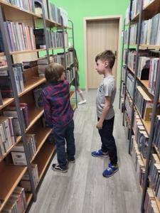 Na zdjęciu znajdują się uczestnicy warsztatów. Dzieci stoją i wykonują zadania. Zdjęcie wykonano w bibliotece.