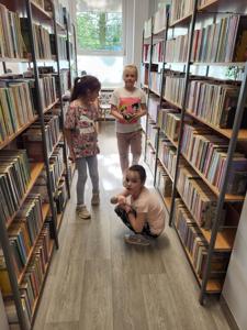 Na zdjęciu znajdują się uczestnicy warsztatów. Dzieci obserwują puszczane na podłodze samochody z klocków. Zdjęcie wykonano w bibliotece.