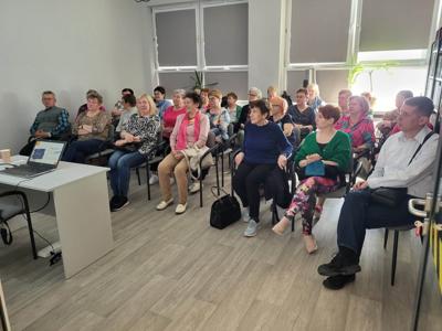 Na zdjęciu znajduje się prowadząca wykład. W tle prezentacja multimedialna. Uczestnicy siedzą na krzesłach.